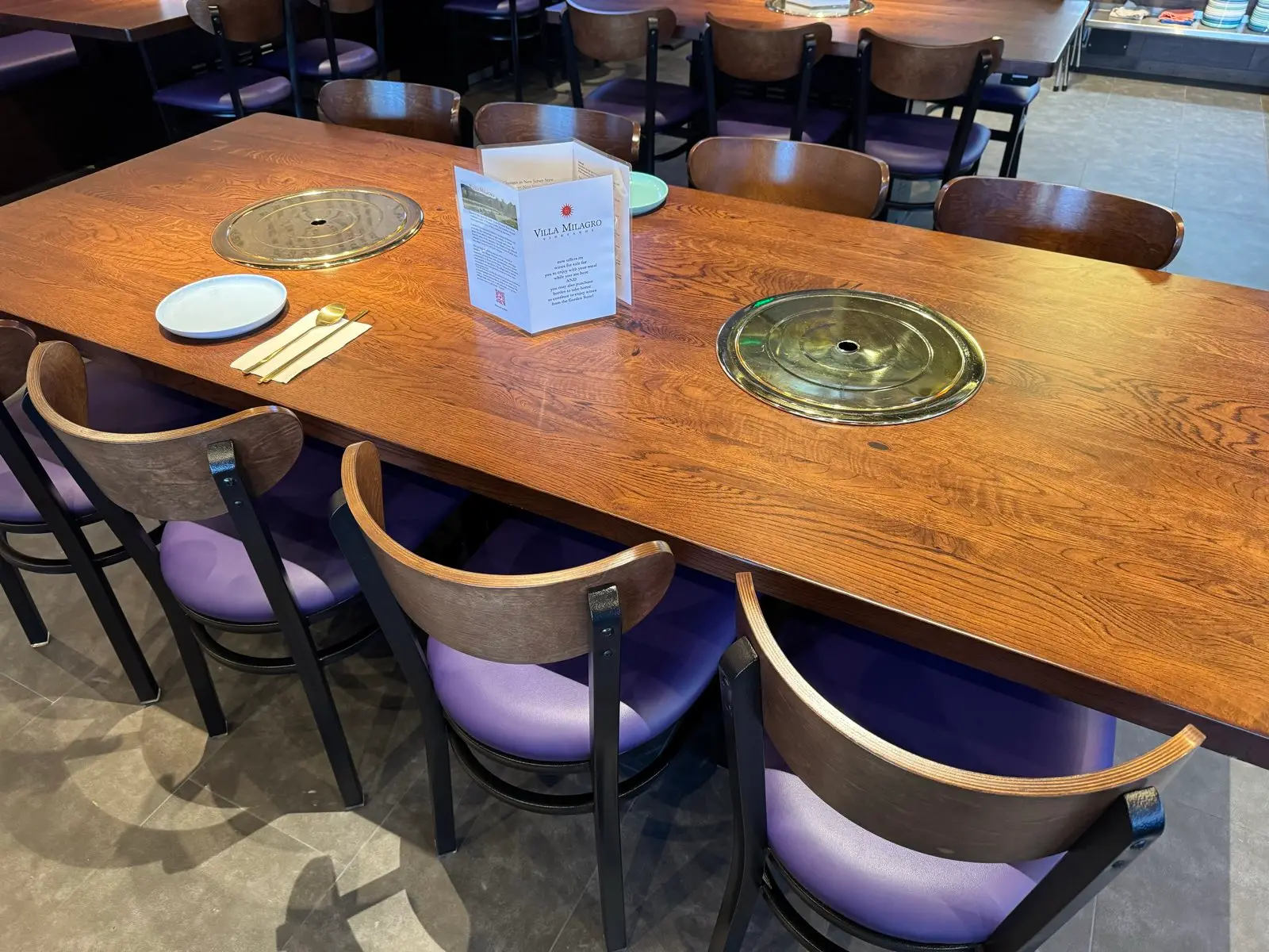 A brass Korean BBQ grill set into an oak table, laid with chopsticks and a side plate