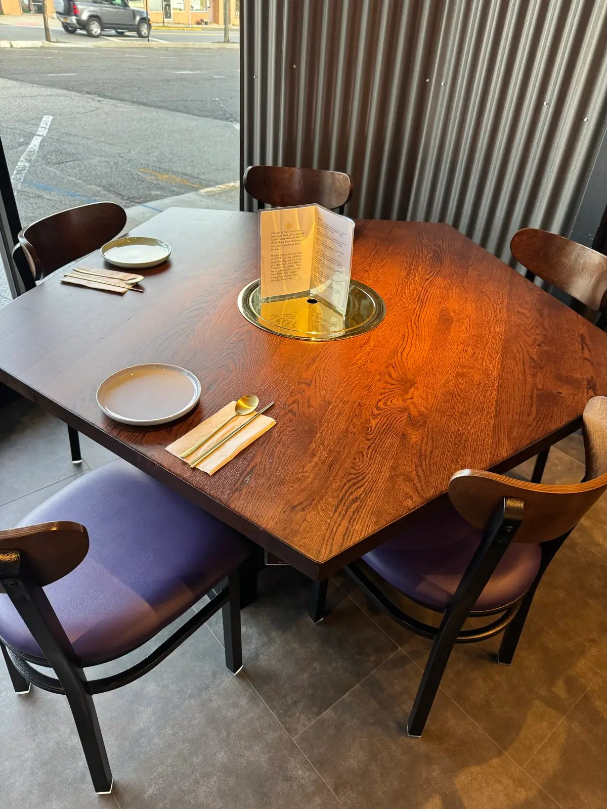 A corner grill table for four beside the window, brass grill plate at its center
